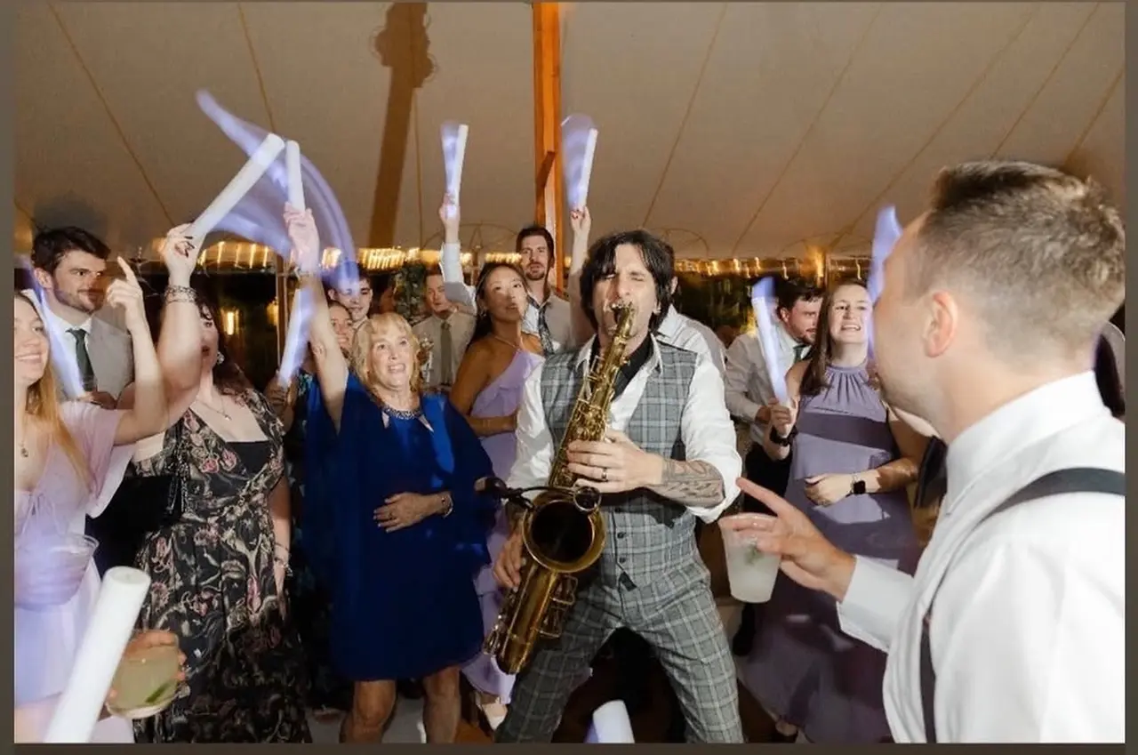 A live saxophone player performing among wedding guests on the dance floor