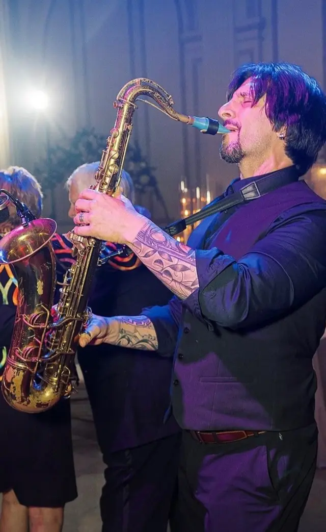 A saxophone player performing under colorful wedding reception lighting